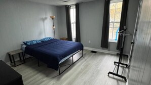 A bedroom with a bed, a desk, a chair, a wardrobe, and a window. - H1-Large 3 Bedroon 1.5 Bathroom apartment (Syracuse)
