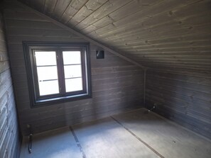 A room with wooden walls, a sloped ceiling, and a window with a black frame.