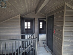 A narrow hallway with wooden walls and a metal railing. There are two doors and a window visible.
