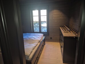A compact bedroom with a bed, a window, and a kitchenette with a stove.