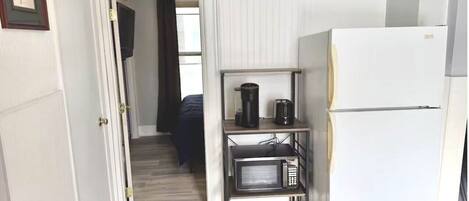 A compact kitchen with a white refrigerator, a microwave, a coffee maker, and a small shelf unit.