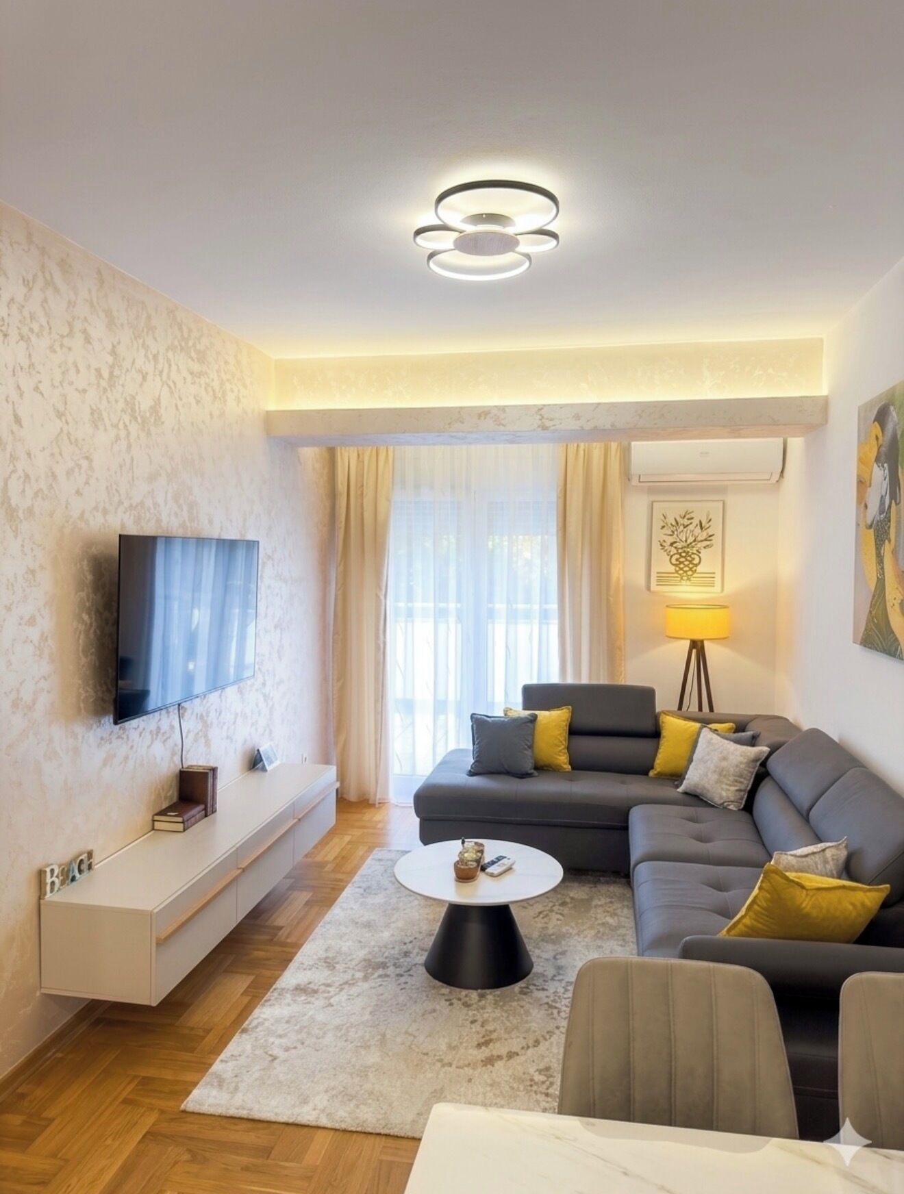 A modern living room with a flat-screen TV, a sofa set, a coffee table, and a lamp.