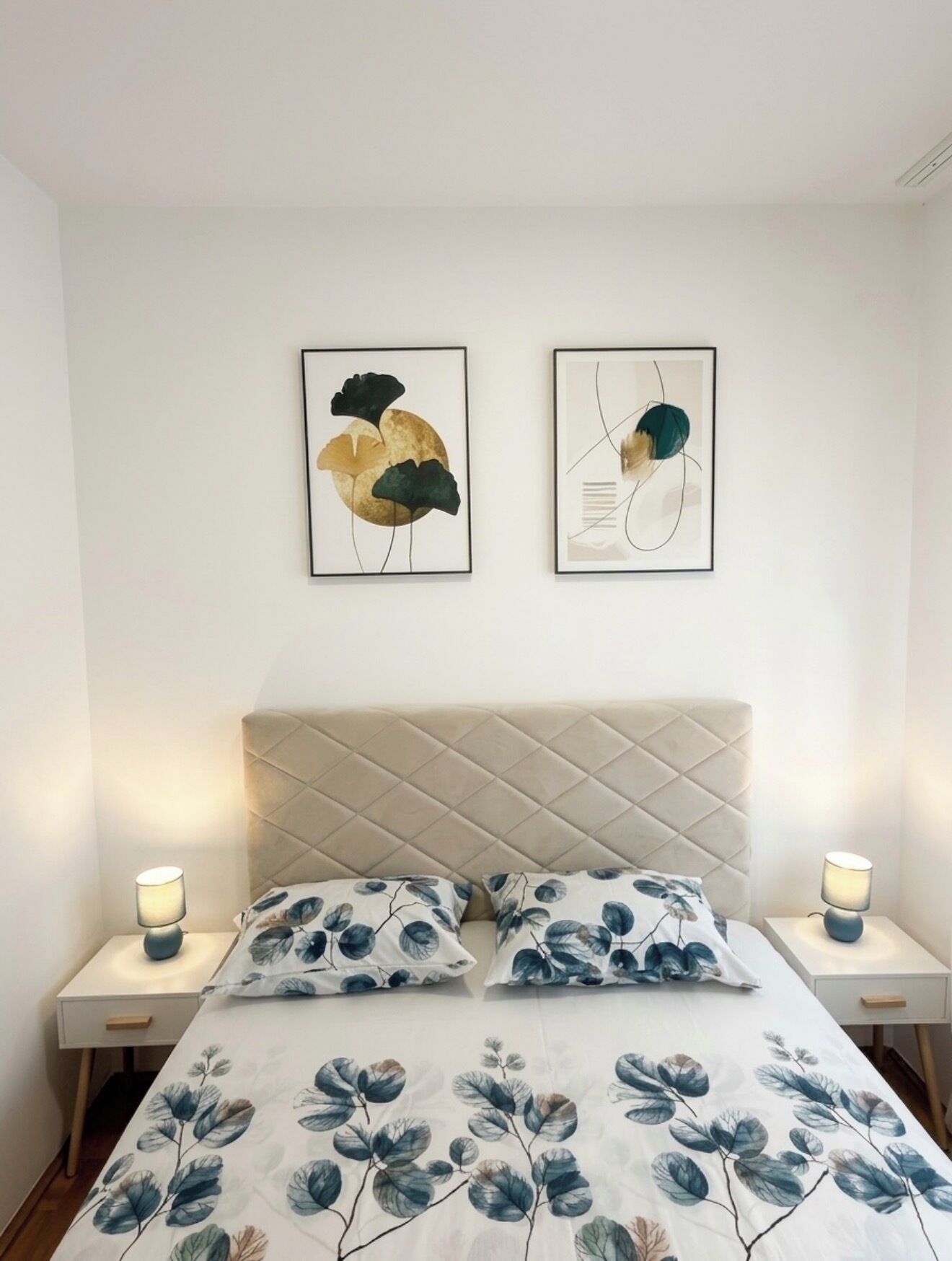 A bedroom with a bed, two nightstands, and two wall-mounted artworks.