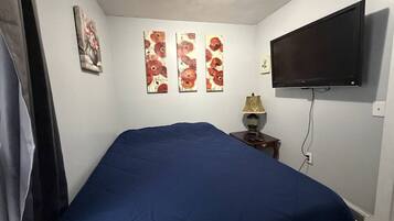 Une chambre à coucher avec un lit, un téléviseur à écran plat et trois tableaux verticaux accrochés au mur.