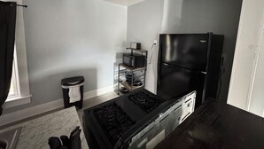 Une cuisine compacte équipée d’une cuisinière à gaz, d’un réfrigérateur noir et d’un four à micro-ondes posé sur une étagère.