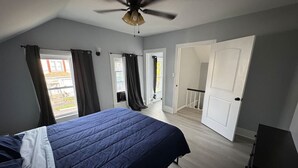 Une chambre à coucher avec un lit, un ventilateur de plafond et une porte donnant sur un balcon.