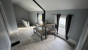 Une pièce avec un plancher en bois, une table à manger avec des chaises, un banc, une fenêtre avec des rideaux et un escalier.