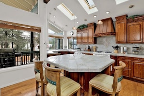 A kitchen with wooden cabinets, a large island, and a dining area with chairs. - Vivienda de Osos #2549 (Fawnskin)