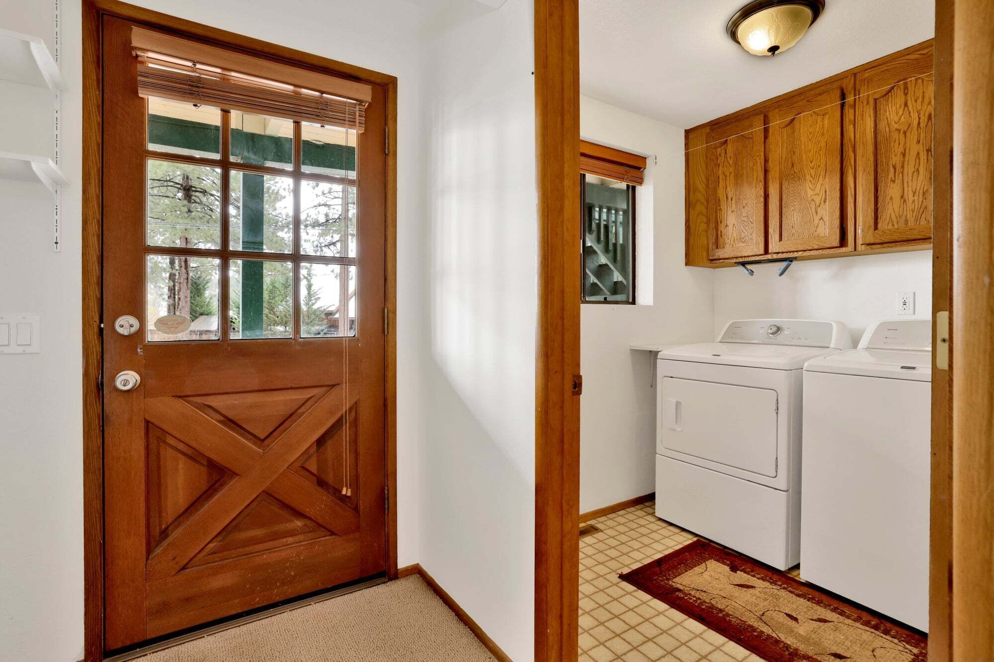 A laundry room with two washing machines, wooden cabinets, and a door with a window.