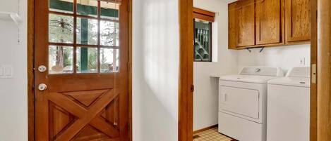 A laundry room with two washing machines, wooden cabinets, and a door with a window.