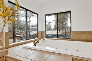 Une salle de bain avec une grande baignoire, deux fenêtres et un vase rempli de fleurs jaunes.
