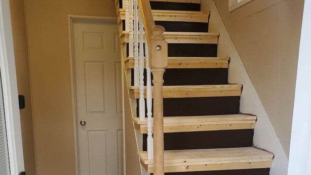 Eine Treppe mit Holzdielen und weißen Spindeln, die zu einer Tür führt.