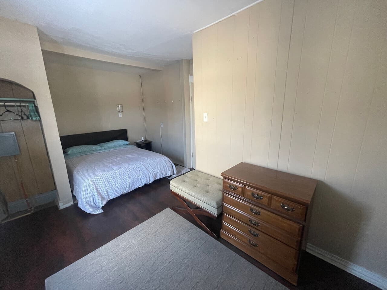 Une chambre à coucher comprenant un lit, une commode, un banc et une porte donnant sur une autre pièce.