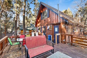 A wooden cabin with a deck, outdoor seating, and a view of the surrounding forest. - Oakwood Cottage #2582 (Sugarloaf)