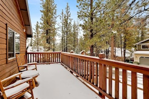 A wooden deck with a railing, a bench, and a view of surrounding trees. - Ceasar Retreat #2584 (Big Bear City)