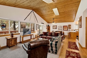A cozy living room with a wooden ceiling, a television, a fireplace, and a dining area. - Ceasar Retreat #2584 (Big Bear City)