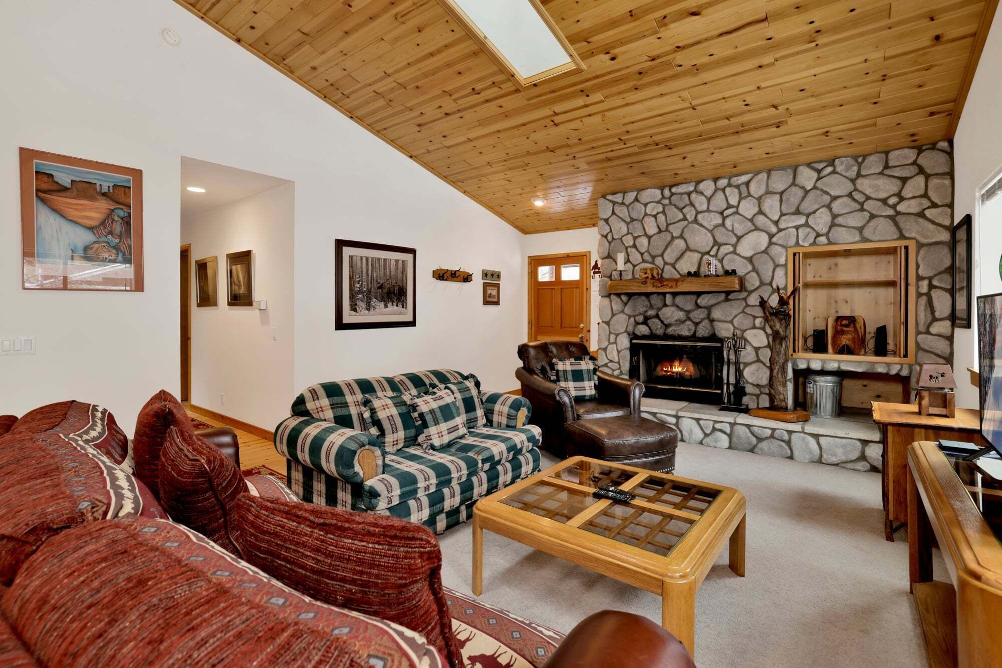 Una sala de estar acogedora con chimenea de piedra, techo de madera y sofá a cuadros.