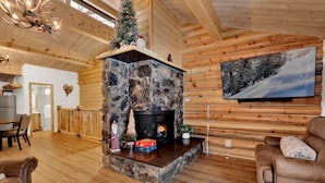 En mysig stuga med en inre inredning som inkluderar en öppen spis i sten, träväggar, en matplats och en tv som är monterad på väggen.
