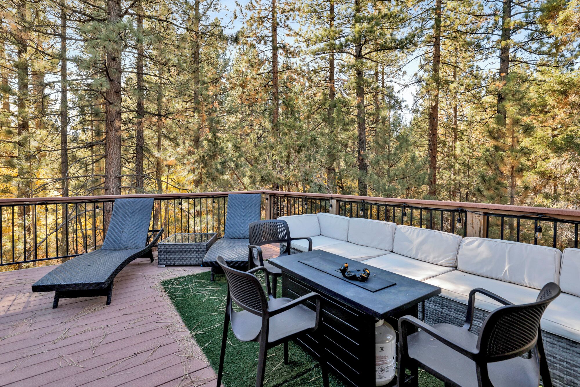 An outdoor deck with a sofa, chairs, and a table, surrounded by a forest.