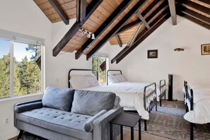 Ein Schlafzimmer mit zwei Betten, einem Schlafsofa, einem Fernseher und einem Fenster mit Blick auf Bäume.