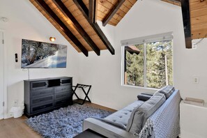 Ein Zimmer mit Fernseher, einer Couch, einem Fenster und einer Decke mit Holzbalken.