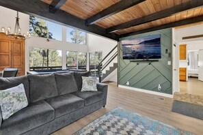 Ein modernes Wohnzimmer mit grauem Sofa, großem Fernseher an einer grünen Wand und Holzboden.