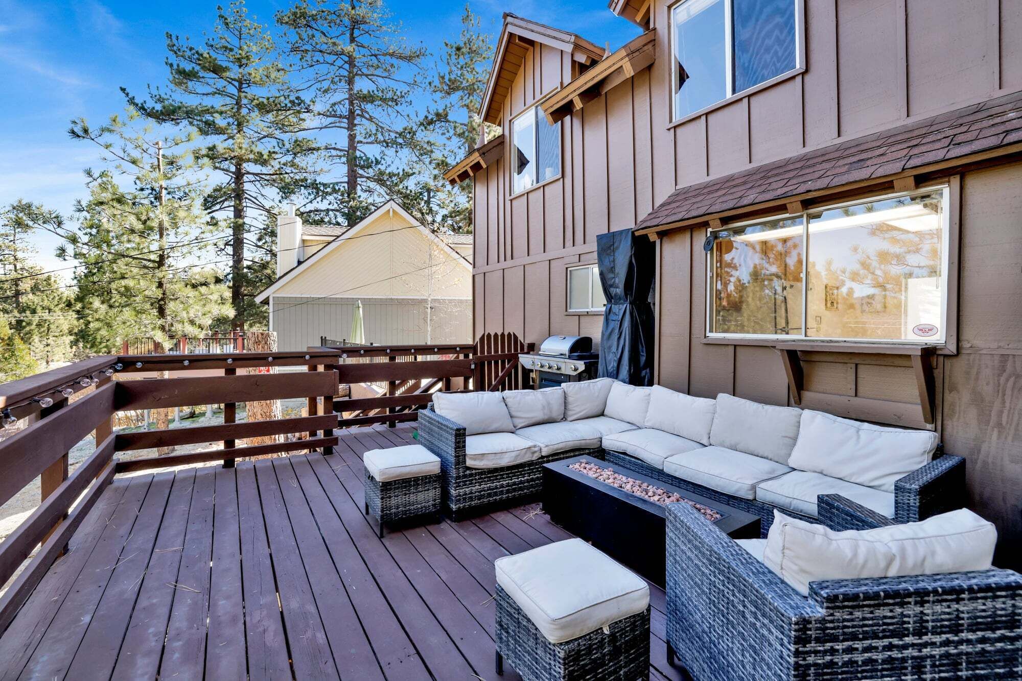 Una terraza de madera con mobiliario exterior, una parrilla de barbacoa y vistas a árboles.