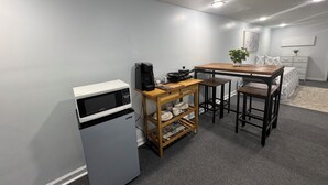 Una kitchenette compacta con microondas, cafetera y pequeña mesa de comedor.