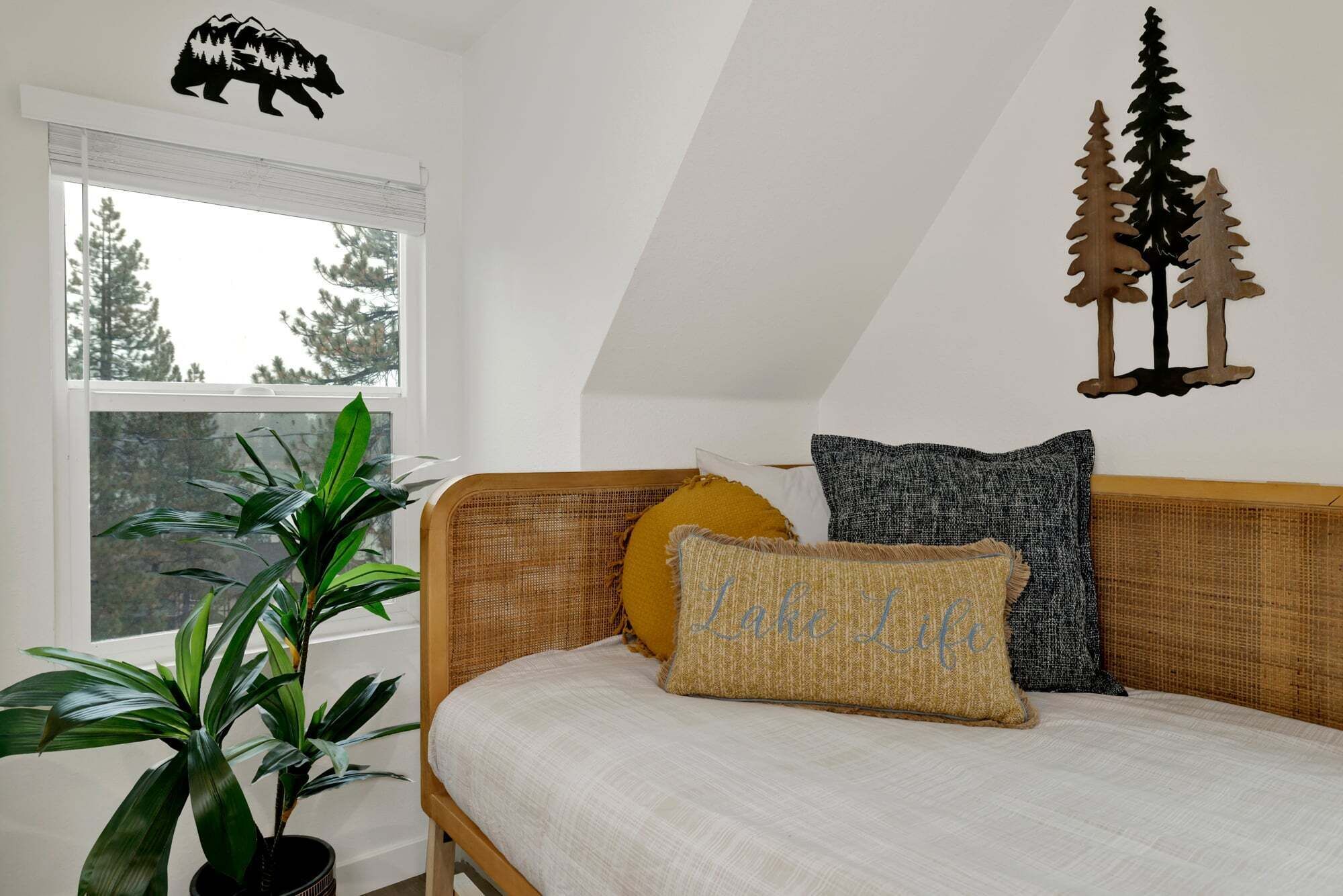 A bedroom with a bed, a window, a potted plant, and wall decorations.