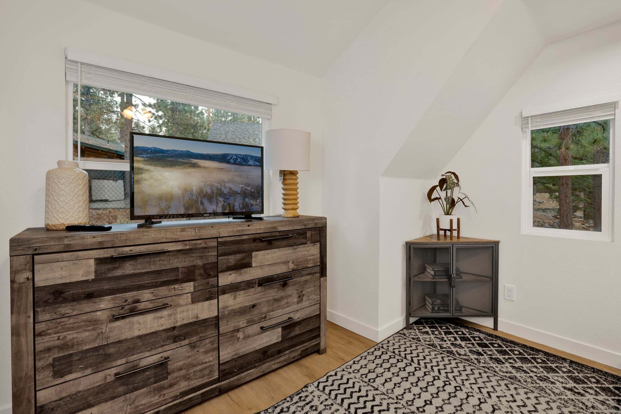 A room with a wooden cabinet, a television, a lamp, and a small cabinet with a plant.
