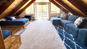 An attic bedroom with a loft bed, a sofa, a small table, and a large window. - 2594-willow Bear Lodge (Big Bear Lake)