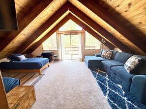 An attic bedroom with a loft bed, a sofa, a small table, and a large window. - 2594-willow Bear Lodge (Big Bear Lake)