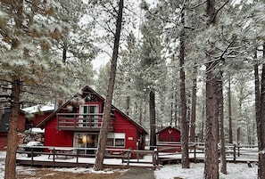Una cabana vermella amb un balcó, envoltada d'alzines altes en un bosc cobert de neu.