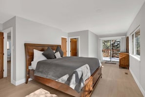 A bedroom with a wooden bed, white walls, and a view of a deck through a glass door. - Pine Woods Retreat #2596 (Big Bear)