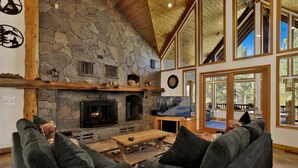 A stone fireplace, a television, and a seating area with a wooden ceiling and large windows. - 2597-the Village Timber Lodge (Big Bear Lake)