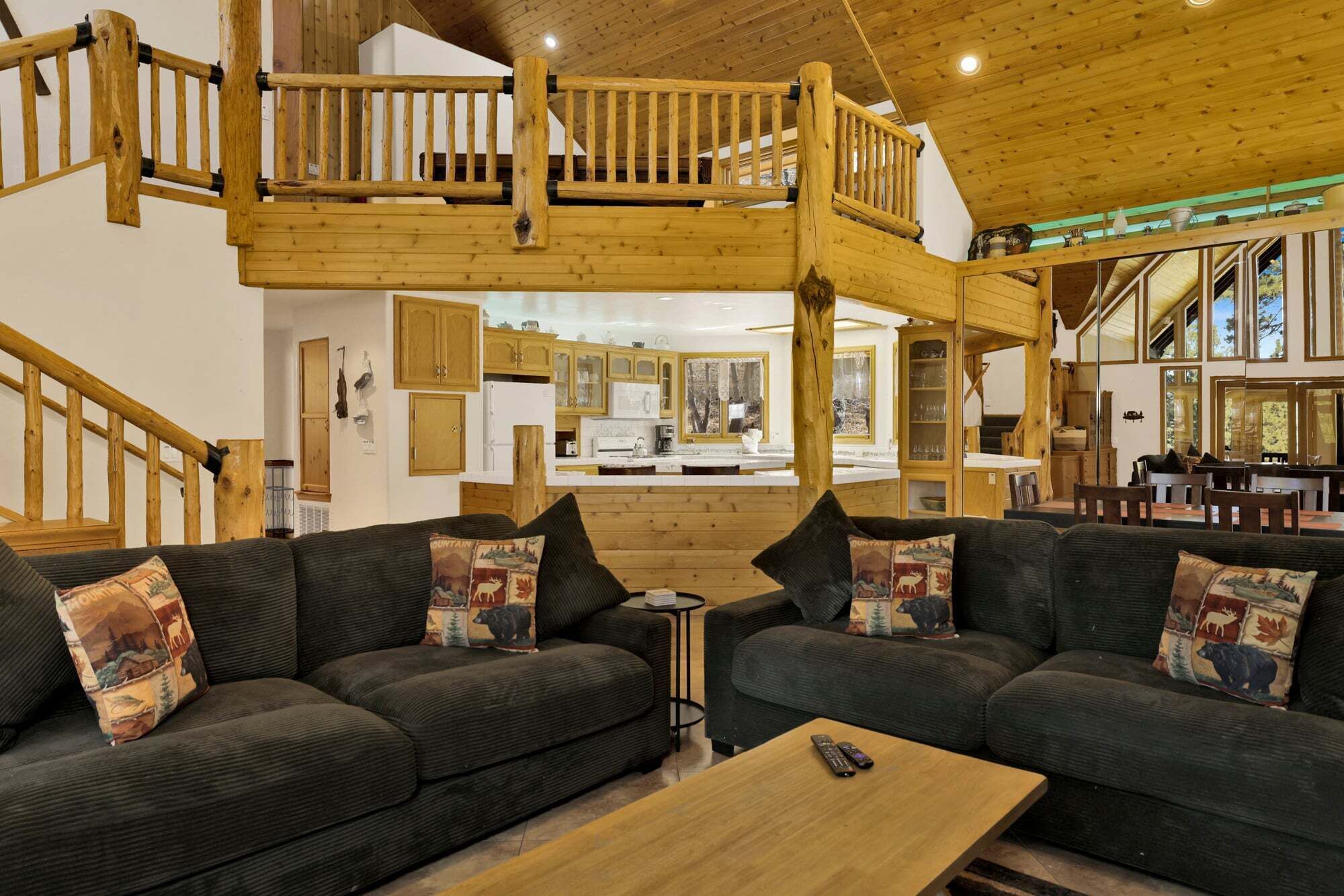 A spacious living area with two dark green sofas, a wooden coffee table, and a wooden staircase leading to an upper level.