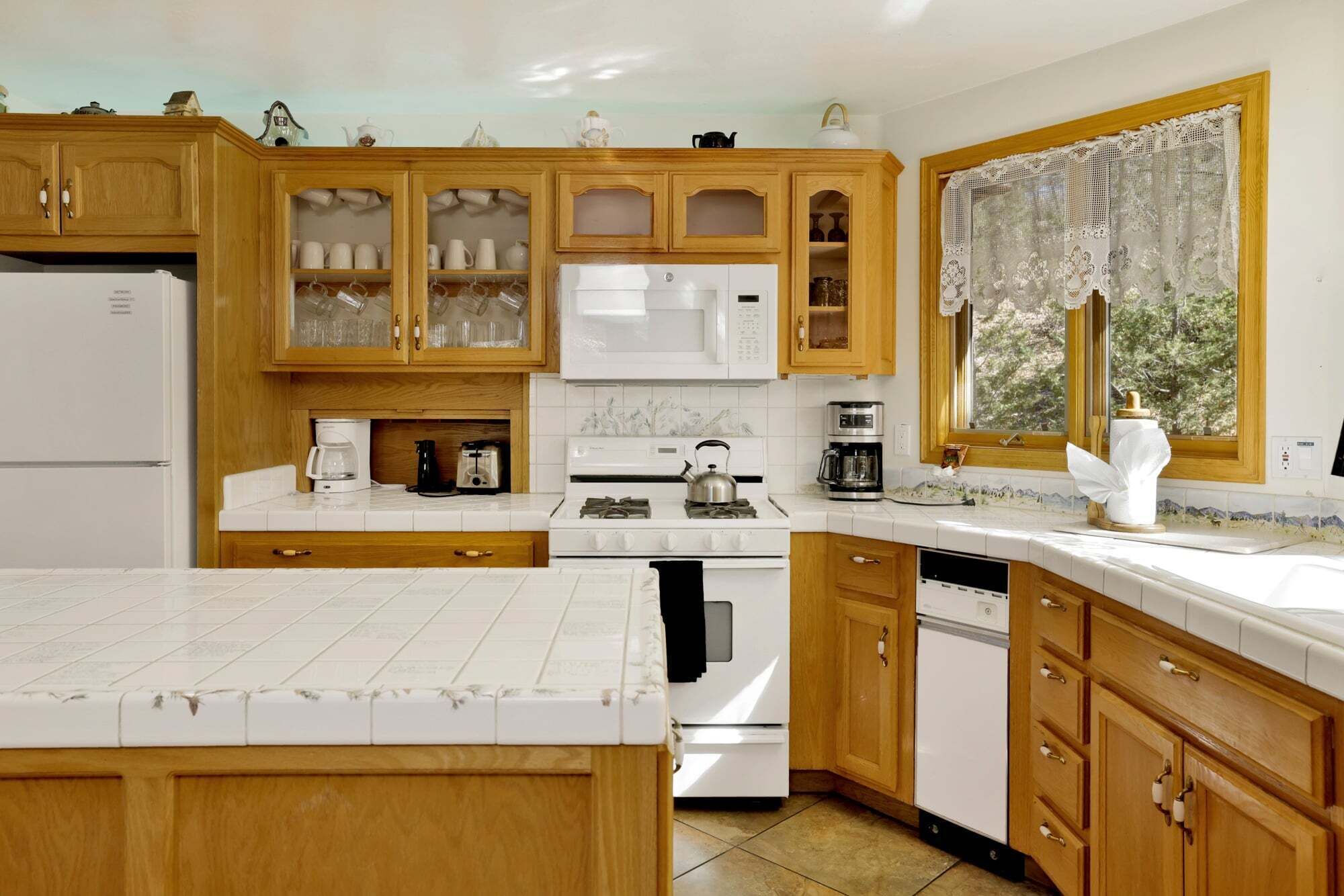 A kitchen with wooden cabinets, a white stove, a microwave, and a window with lace curtains.