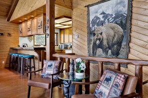 A wooden interior with a bar area, seating with patterned cushions, and a large bear-themed painting. - 2600-the Tree Top Cabin (Big Bear Lake)