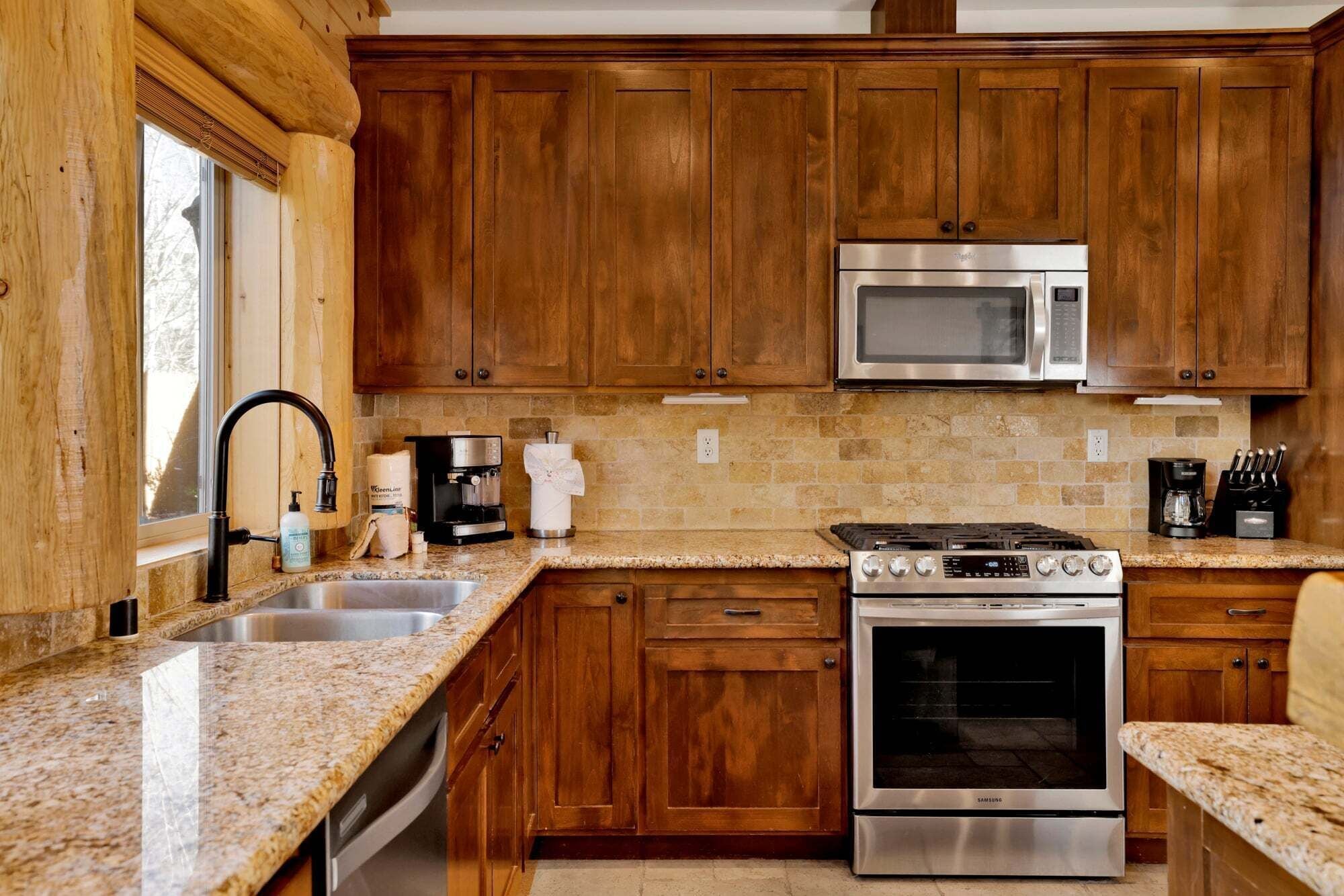 A kitchen with wooden cabinets, a stainless steel microwave, a gas stove, and granite countertops.