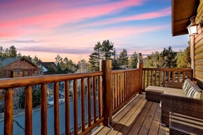 Eine Holzterrasse mit Geländer, einem Korbsessel und Blick auf einen bewaldeten Bereich.