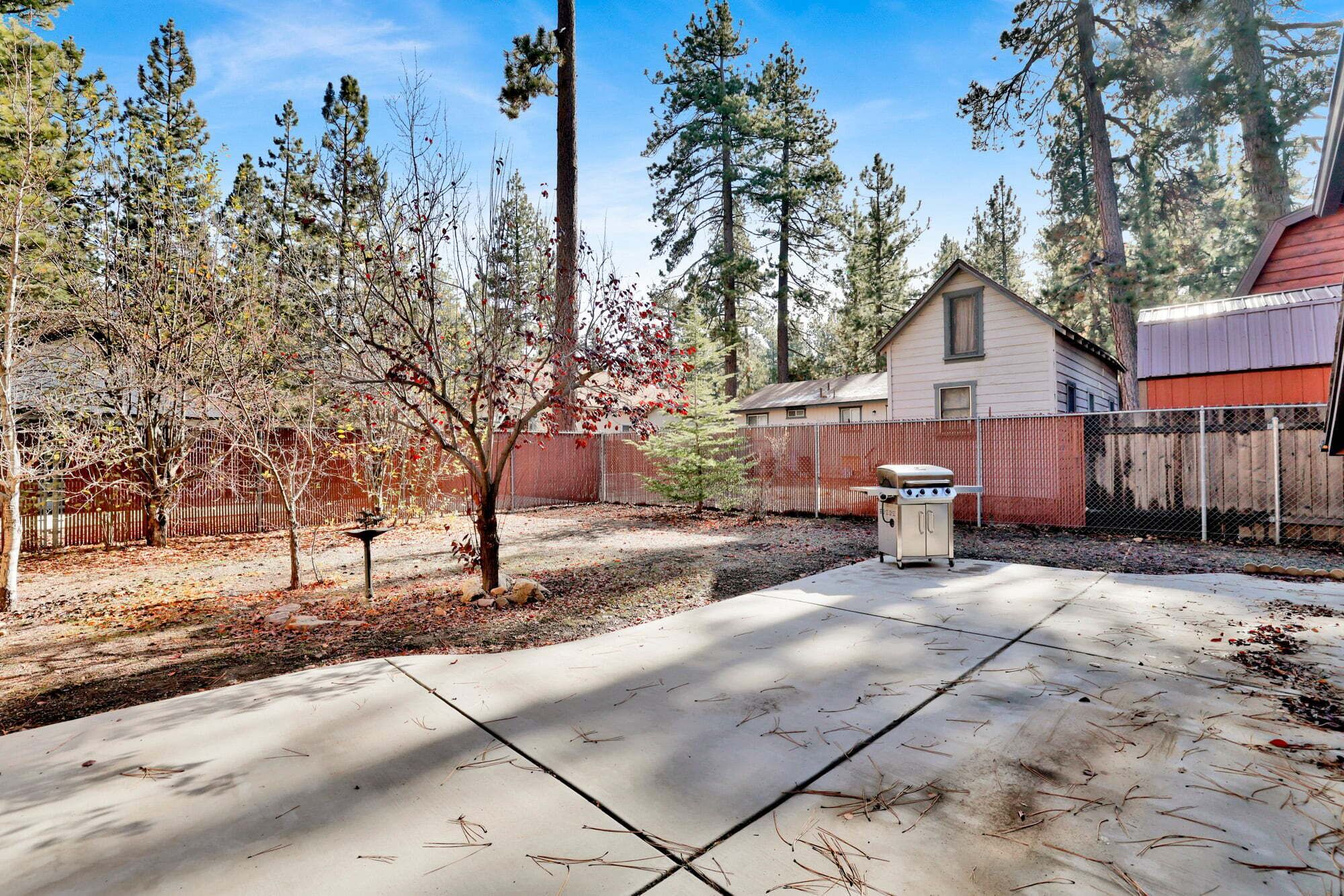 A backyard with a patio, a barbecue grill, a shed, and a fence.