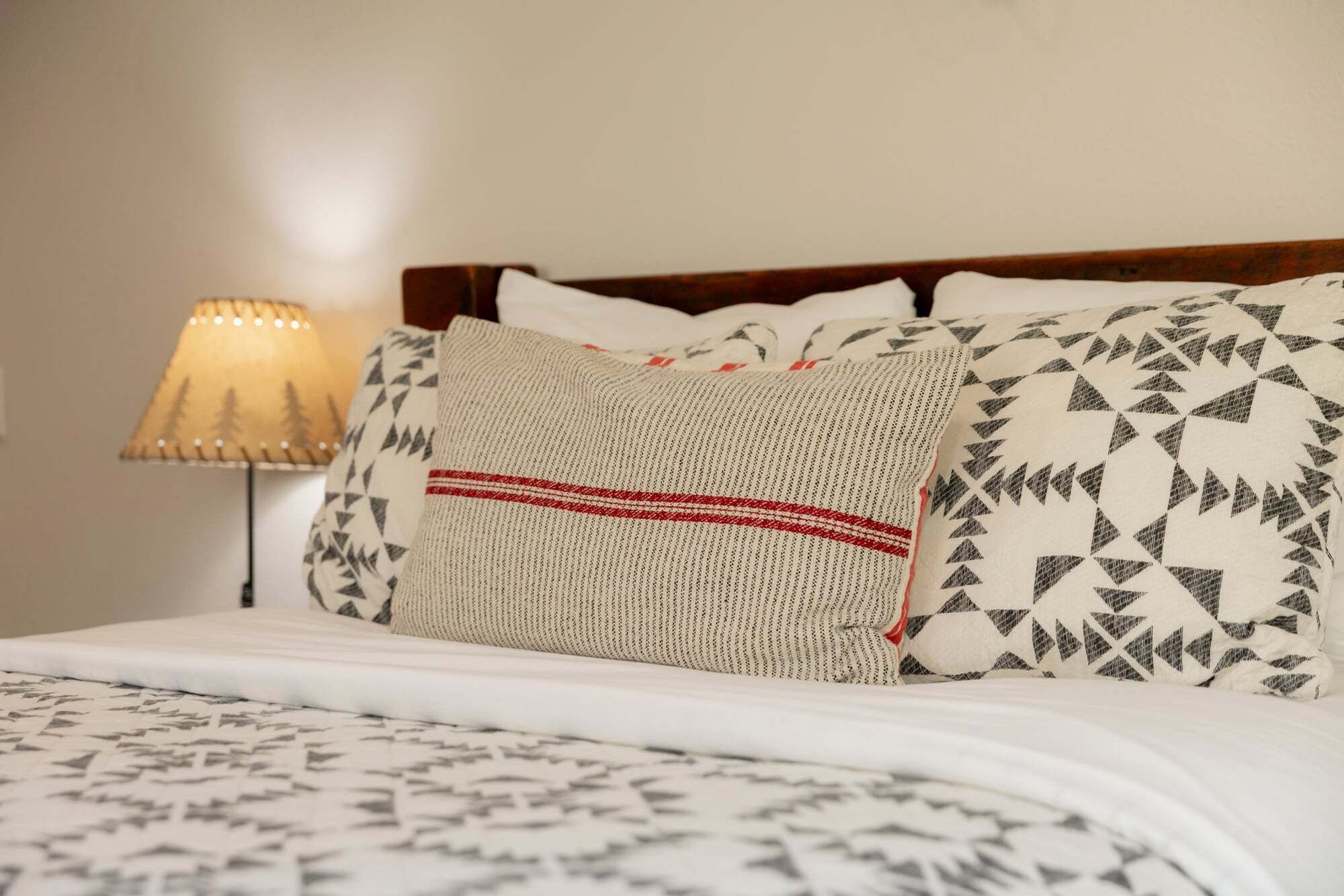 Een net opgemaakt bed met beddengoed met een patroon, een houten hoofdbord en een lamp ernaast.