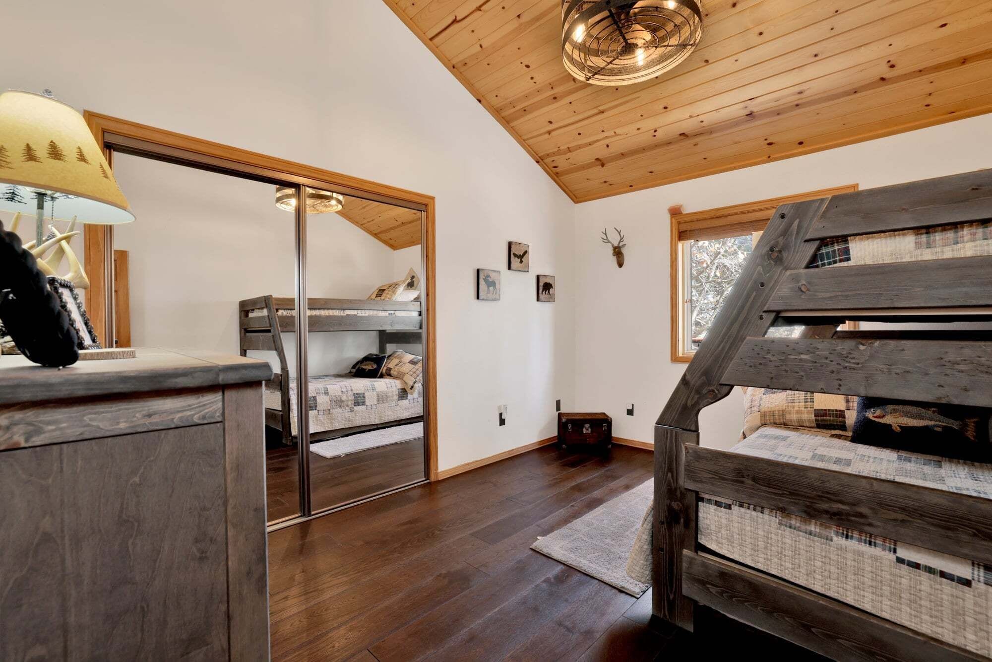 A room with wooden bunk beds, a desk with a lamp, and a mirror.