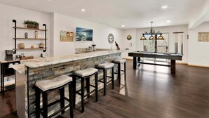 Una cucina moderna con angolo bar, sgabelli da bar in legno, tavolo da biliardo e vista sull'esterno.