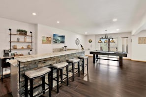 A modern kitchen with a bar area, wooden bar stools, a pool table, and a view of the outdoors. - 2606-view on the Rocks (Big Bear Lake)