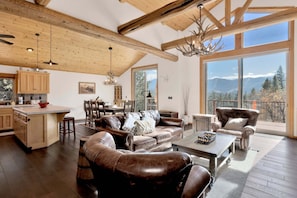 A spacious living area with a leather sofa, a dining table, and a kitchen with wooden beams. - 2606-view on the Rocks (Big Bear Lake)