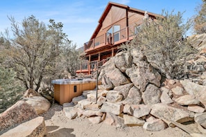 A wooden cabin with a hot tub, surrounded by large rocks and sparse vegetation. - 2606-view on the Rocks (Big Bear Lake)