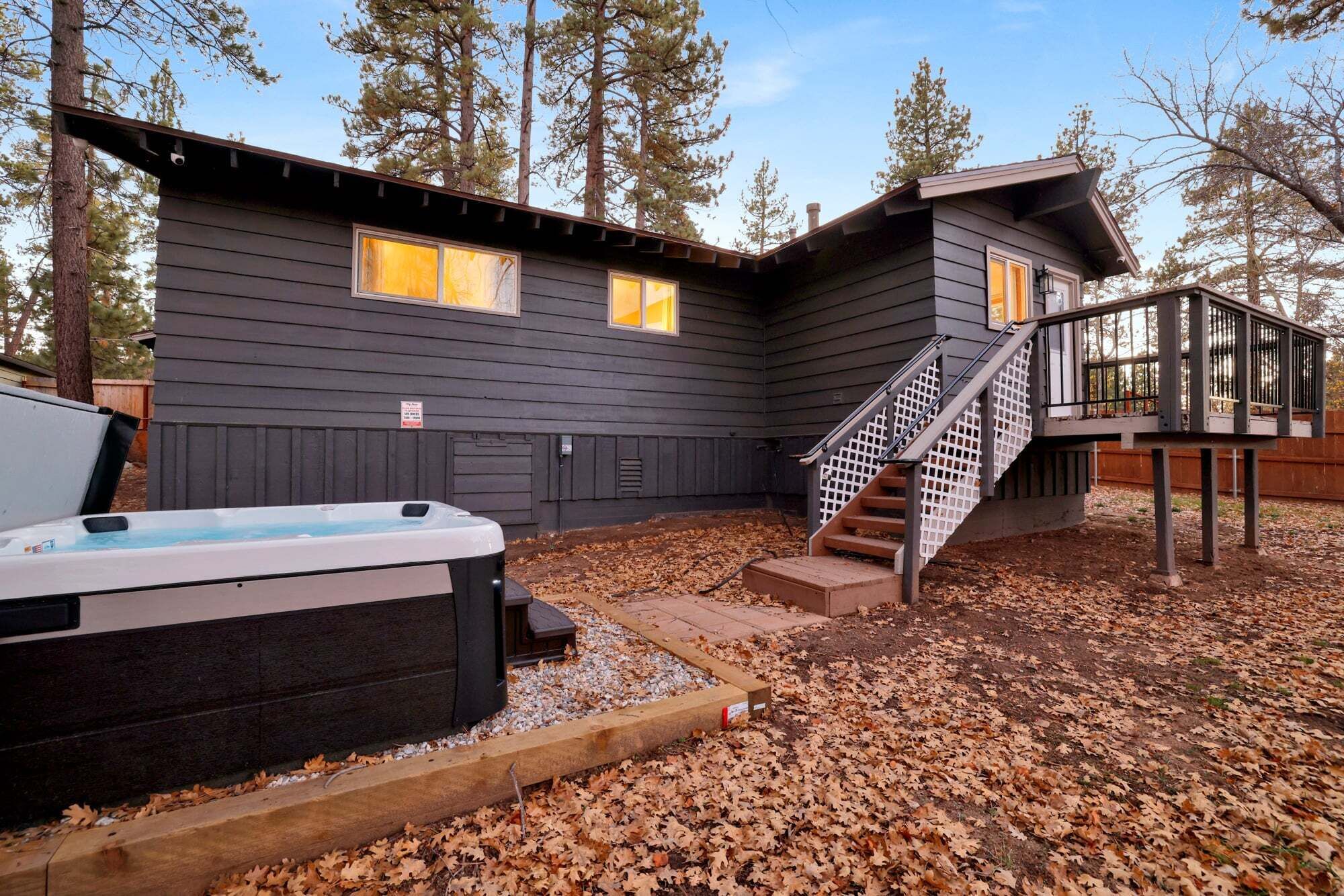 A cabin with a hot tub, wooden deck, and a staircase leading to a second level.