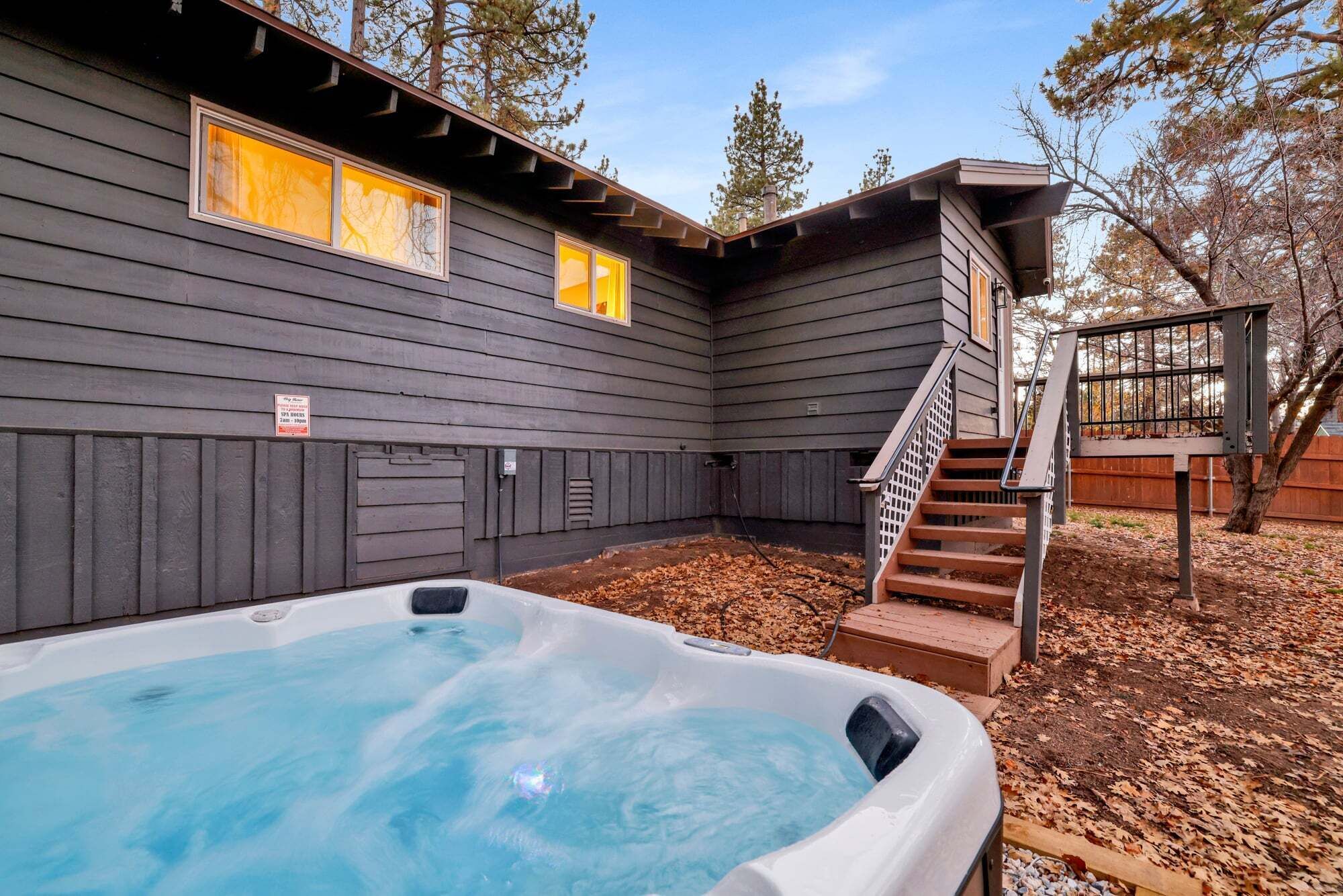 Un bain à remous installé dans un jardin, avec une terrasse en bois et des escaliers menant à un espace abrité.