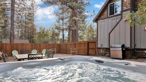 Un patio trasero con un jacuzzi, terraza de madera y una parrilla.